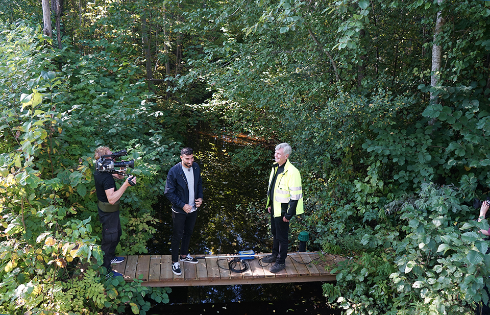 Michael Nilsson blir intervjuad av en programledare från Utbildningsradion, programledaren och Mikael står på en liten träbro över Pråmån